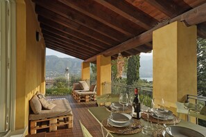 A covered outdoor seating area with a table set for dining, overlooking a mountainous landscape. - Cisano Holiday Apartment (San Felice del Benaco)