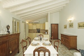 A dining room with a long table set for six, flanked by wooden cabinets and a kitchen in the background. - Cisano Holiday Apartment (San Felice del Benaco)