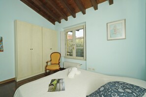 A bedroom with a bed, a chair, a radiator, and a window. - Cisano Holiday Apartment (San Felice del Benaco)