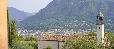 A view of a town with a prominent bell tower, surrounded by greenery and mountains.