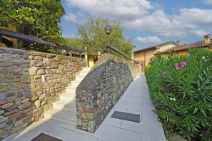 A stone staircase leading to a building entrance, surrounded by greenery and a clear sky. - Cisano Holiday Apartment (San Felice del Benaco)