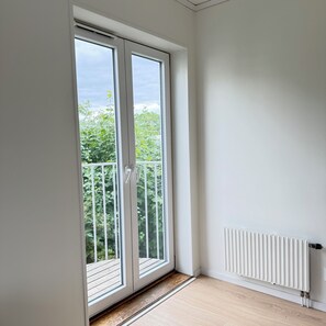 Una habitación con un gran ventanal corredero que da a un balcón con barandilla blanca.