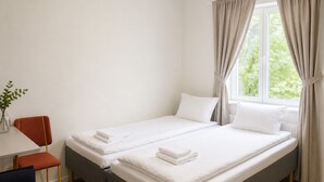 A hotel room with two beds, a desk, a chair, and a window with curtains. - Bokloster Longstay (Stockholms län)