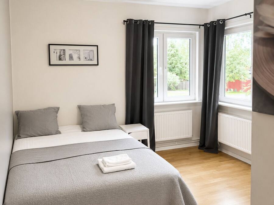 Un dormitorio con cama, mesita de noche, ventana con cortinas y radiador.