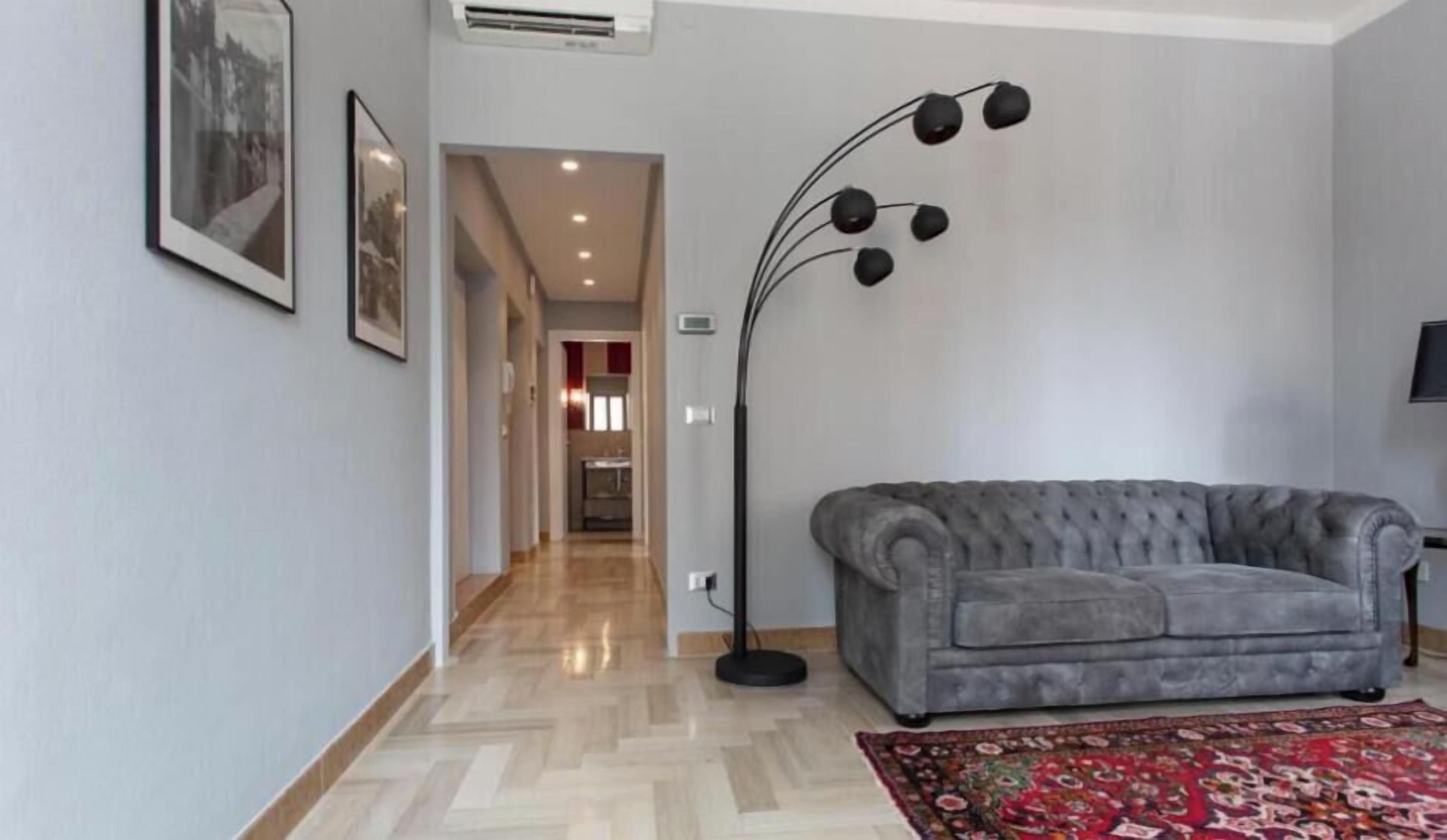 A modern living room with a grey sofa, a floor lamp, and a patterned rug.