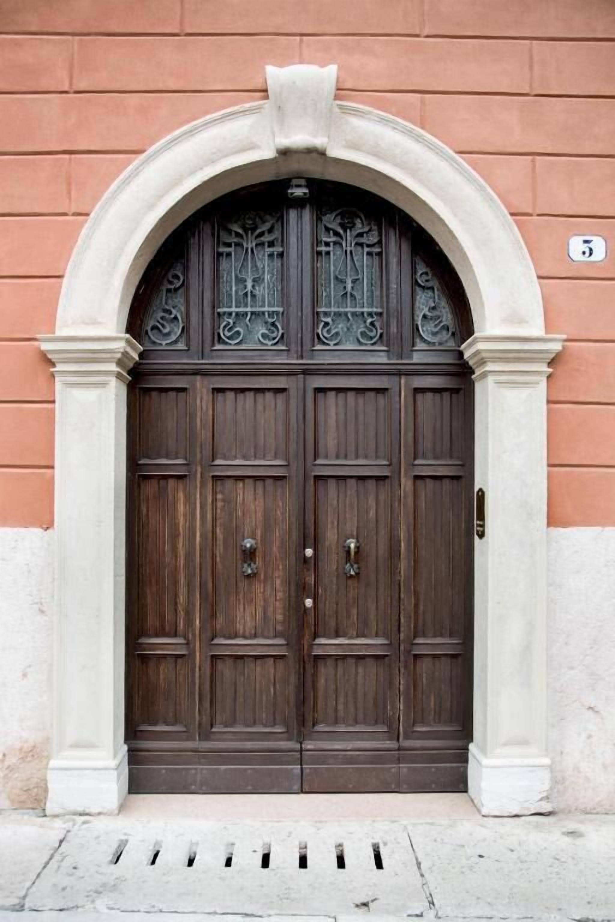 Una puerta doble de madera con un arco decorativo, ubicada en un edificio de fachada de ladrillo.