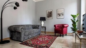 A living room with a grey sofa, a red armchair, a black floor lamp, a patterned rug, and two framed pictures on the wall. - Residenza Duomo3 Apartments (Verona)