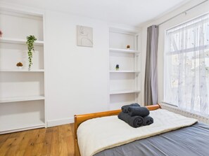 Ein Schlafzimmer mit einem Bett, Holzboden, weißen Wänden und einem Fenster mit Vorhängen.
