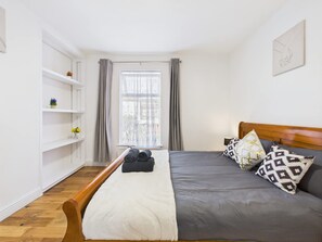 Ein Schlafzimmer mit einem Bett, einem hölzernen Kopfteil, einer weißen Schrankwand und einem Fenster mit Vorhängen.