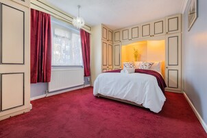 Un dormitorio con cama, cortinas rojas, un radiador y una ventana.
