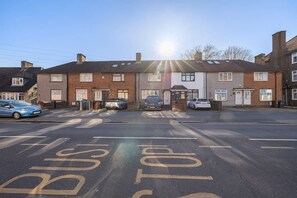 A residential street with houses, parked cars, and a road with 'BUSH STOP' markings.