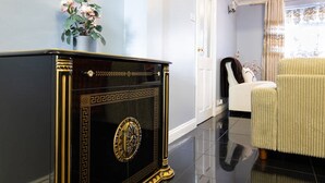 A room with a black and gold ornate cabinet, a white chair, and a vase with flowers on a wall.