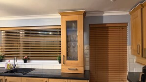 A kitchen with wooden cabinets, a glass-fronted cabinet, and a window with blinds.