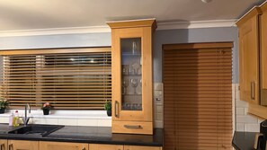 A kitchen with wooden cabinets, a glass-fronted cabinet, and a window with blinds.
