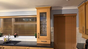 A kitchen with wooden cabinets, a glass-fronted cabinet, and a window with blinds.