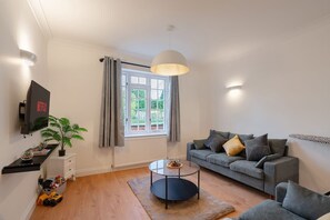 A modern living room with a grey sofa, a coffee table, a TV mounted on the wall, and a window with curtains. - 3BR House w Parking Family-friendly Sleeps 8 (London)