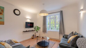 Ein Wohnzimmer mit zwei Sofas, einem Couchtisch, einem Fernseher, einer Pflanze und einem Fenster mit Vorhängen.