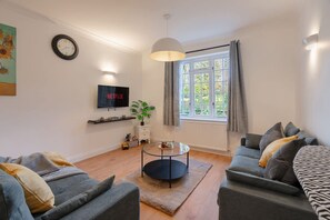 A living room with two sofas, a coffee table, a TV, a plant, and a window with curtains. - 3BR House w Parking Family-friendly Sleeps 8 (London)