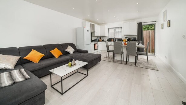 A modern living room with a sofa, coffee table, and a dining area with chairs and a table. - Comfy 3BR House Near Tottenham Stadium Parking (London)