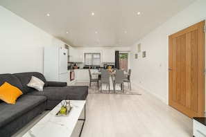 A modern living room with a sofa, coffee table, and dining area with chairs. - Comfy 3BR House Near Tottenham Stadium Parking (London)