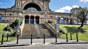 A grand entrance with steps leading up to a building with a large arched doorway and a sign reading 'Palm Court Entrance'. - Specious 2BR Family Home Parking Sleeps 6 (London)