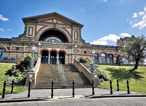 Ein prachtvoller Eingangsbereich mit Stufen, die zu einem Gebäude mit einem großen Rundbogenportal und einem Schild mit der Aufschrift 'Palm Court Entrance' führen.