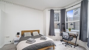 A bedroom with a bed, bedside table, lamp, desk, chair, and a view of the outside. - Specious 2BR Family Home Parking Sleeps 6 (London)