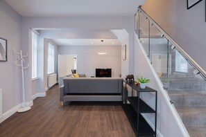 Ein modernes Wohnzimmer mit einem grauen Sofa, einem Flachbildfernseher und einer Treppe mit Glasgeländern.