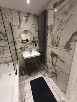 Ein modernes Badezimmer mit Marmorboden, einer Duschkabine aus Glas, einem weißen Waschbecken und einer schwarzen Badmatte.