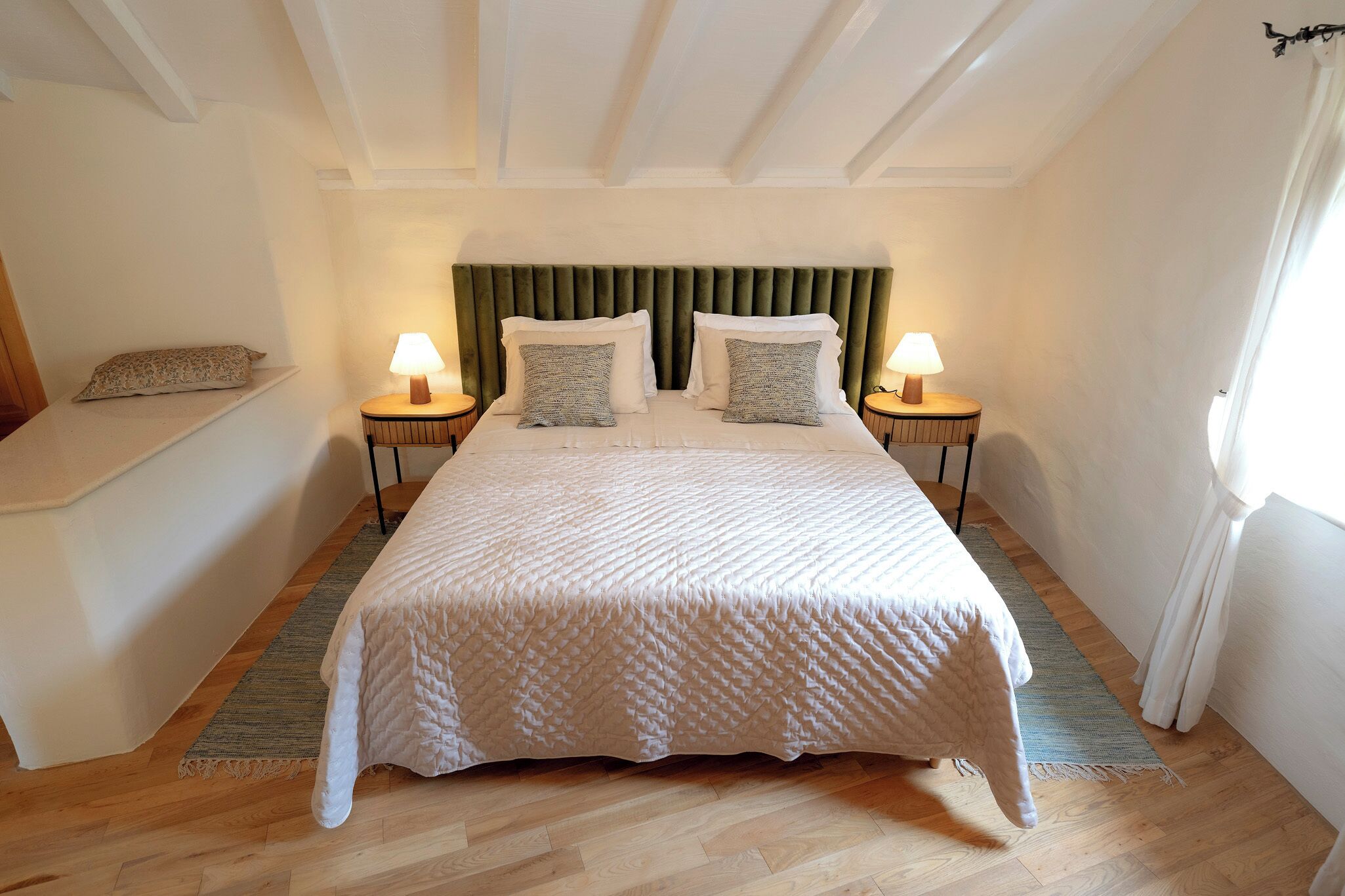 Een slaapkamer met een bed, twee nachtkastjes met lampen, een bankje en een hoofdbord.