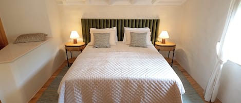 Un dormitorio con una cama, dos mesitas de noche con lámparas, un banco y un cabecero.