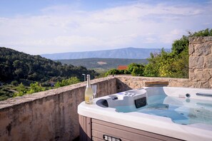 Ein Whirlpool mit einer Weinflasche und Gläsern auf einem Balkon mit Blick auf eine Berglandschaft.