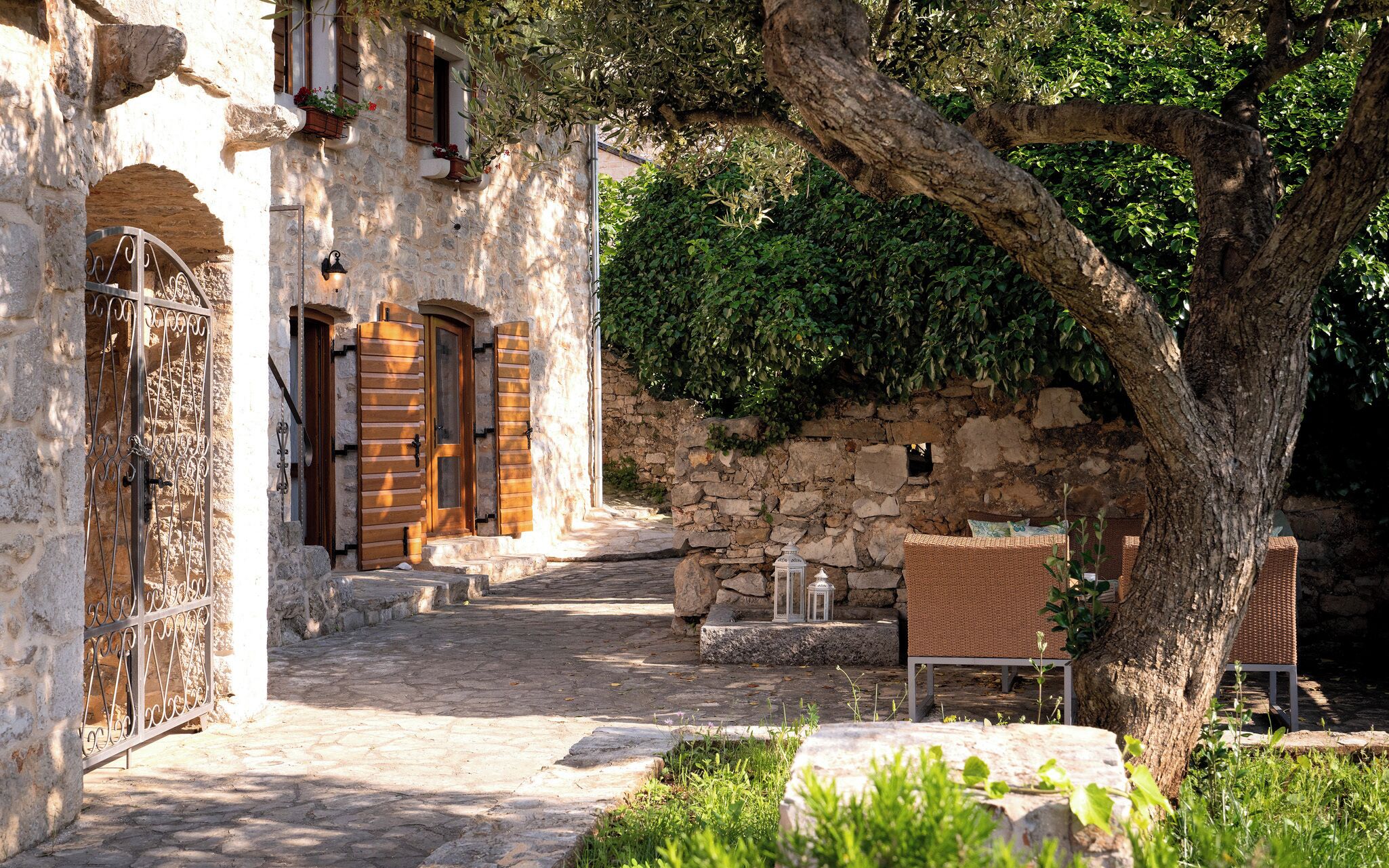 Un edificio de piedra con patio, un árbol y mobiliario exterior.