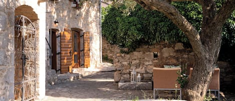 Un edificio de piedra con patio, un árbol y mobiliario exterior.