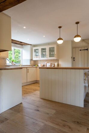 A modern kitchen with white cabinetry, a central island, and pendant lighting. - K Suites - Cozy Rural 1 bed Cottage w/ Garden views (Cheltenham)