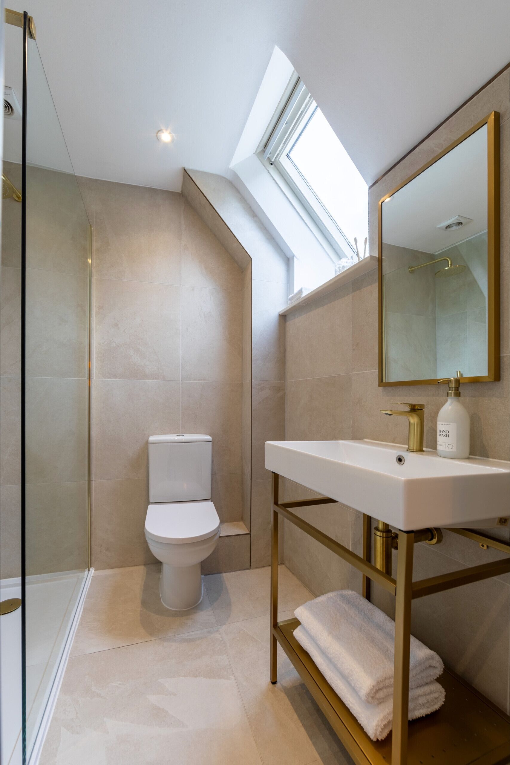 A modern bathroom with a skylight, a toilet, a sink with a gold frame, and a mirror.