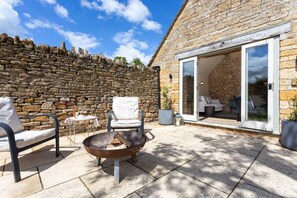 A stone wall, outdoor seating with chairs and a fire pit, and a glass door leading to a room. - K Suites - Cozy Rural 1 bed Cottage w/ Garden views (Cheltenham)
