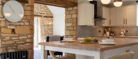 A kitchen with a stone wall, wooden beams, a round clock, pendant lights, and a bar area with stools.