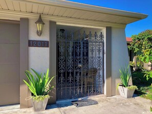 Un edificio residencial con un portón metálico, una placa con número y plantas en macetas.