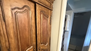 Un pasillo con un armario de madera, piso de baldosas y una puerta que da a una habitación con ventilador de techo.