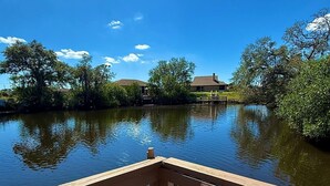 Una terraza de madera con barandilla que da a una masa de agua tranquila, rodeada de árboles y un cielo despejado.