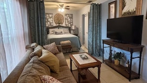 Sala de estar con sofá, una mesita de centro, televisor sobre un mueble y una cama con cortinas.
