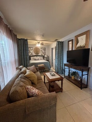 A living room with a sofa, a coffee table, a TV on a stand, and a bed with curtains. - Waterfront Warm Mineral Springs Getaway (North Port)