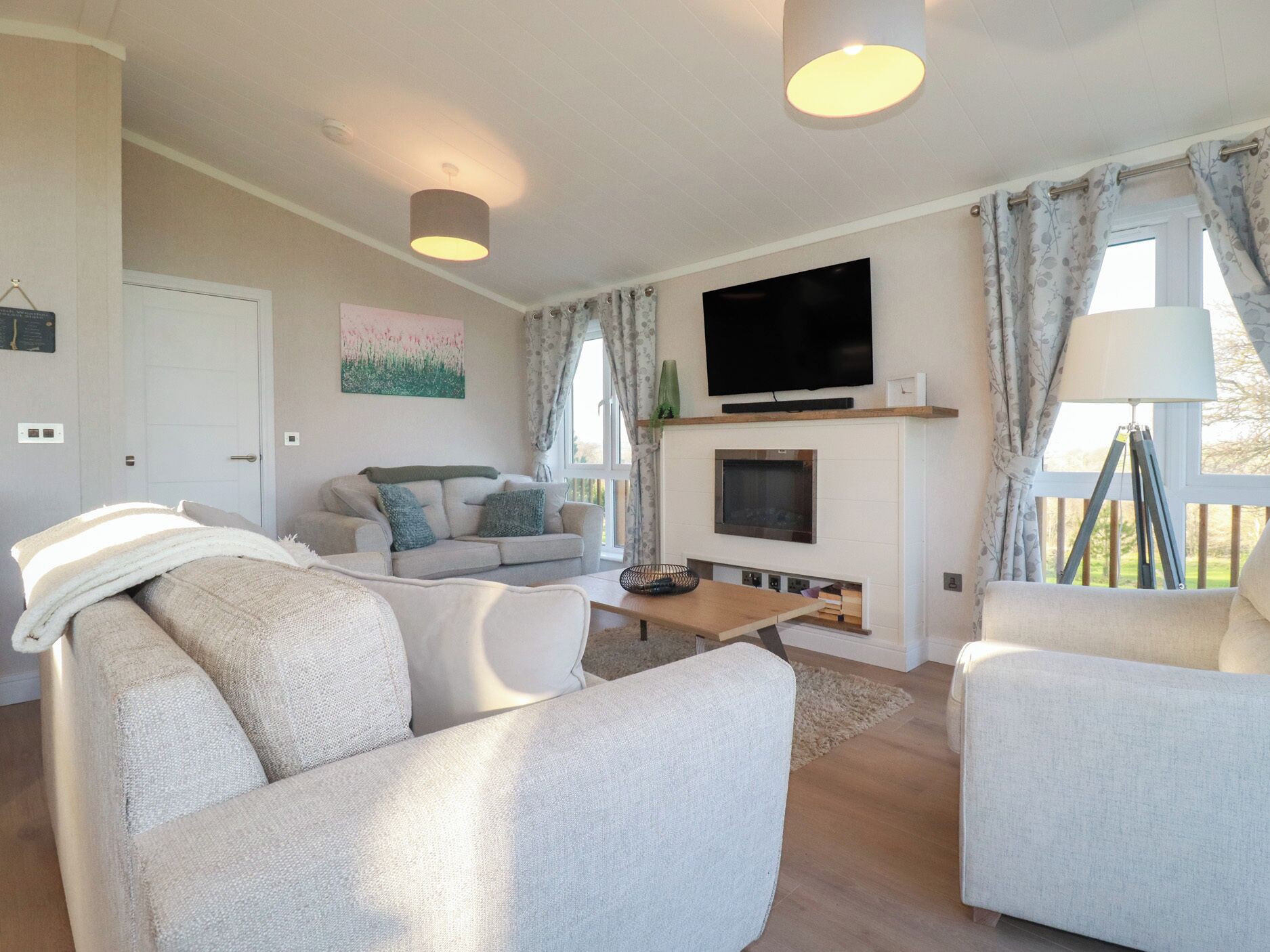 Una sala de estar moderna con un conjunto de sofás, un televisor de pantalla plana sobre la chimenea y una ventana con cortinas.