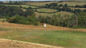 A golf course with a flagstick on a green, surrounded by rolling hills and trees.