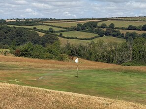 A golf course with a flagstick on a green, surrounded by rolling hills and trees.