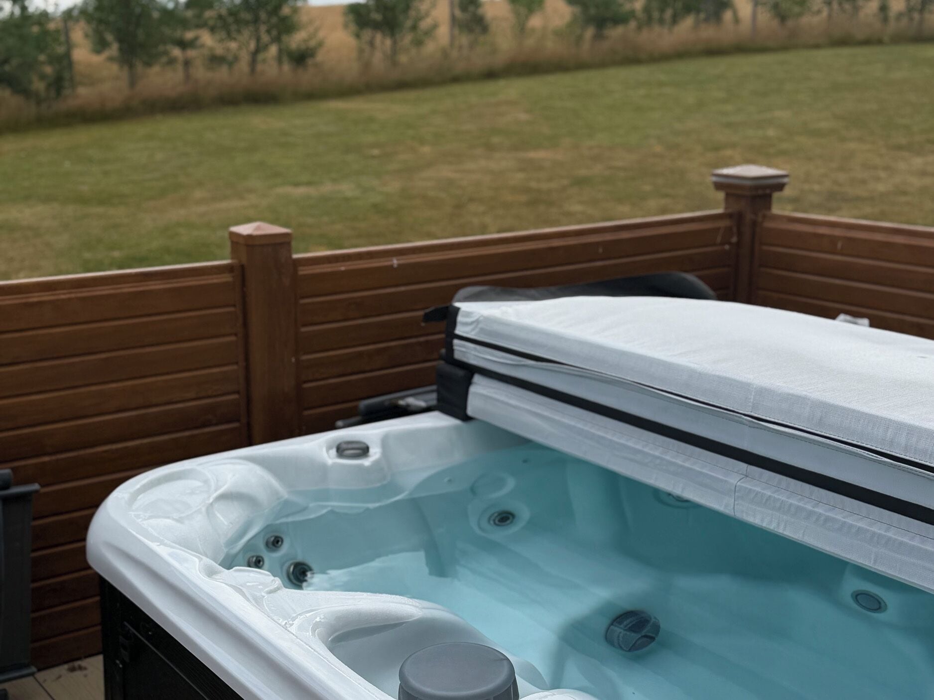 Un jacuzzi con una terraza de madera y un jardín césped al fondo.