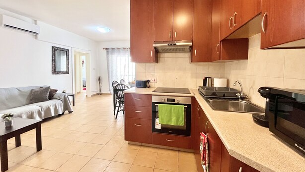 A compact kitchen with wooden cabinets, a built-in oven, a microwave, and a sink. - 38 AN - Stay Malanda Sun Apartment (Ayia Napa)