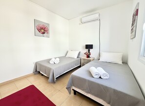 Ein Hotelzimmer mit zwei Einzelbetten, einem roten Teppich, einer Wandklimaanlage und einem Blumenbild.