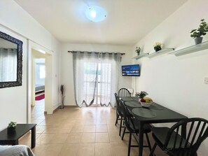 Ein Essbereich mit Tisch und Stühlen, einem an der Wand montierten Fernseher und einer Topfpflanze auf einem Regal.